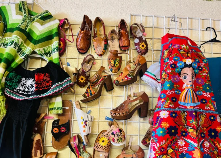 Colorful embroidered clothing, artisan handbags, and handcrafted leather shoes displayed inside Alma Artesanal in Hatch, New Mexico